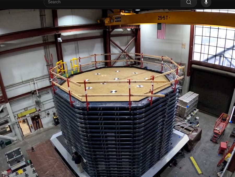 Large-scale geotechnical testing apparatus, known as a soil box, inside a laboratory with steel framing, safety railings, and a crane overhead.