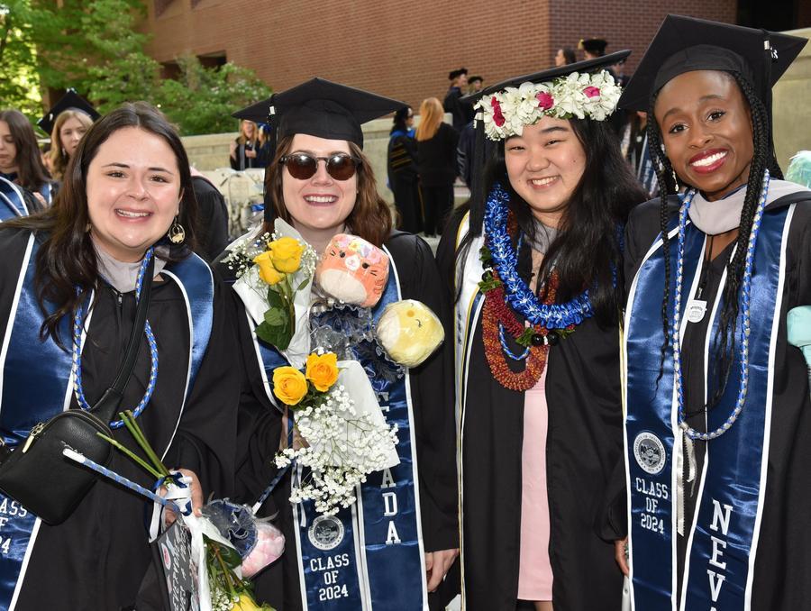 Four students pose in regalia outdoors, smiling.