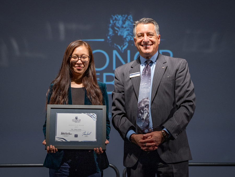 Ying Yang and Brian Sandoval smile for a photo, with Yang holding a framed certificate.
