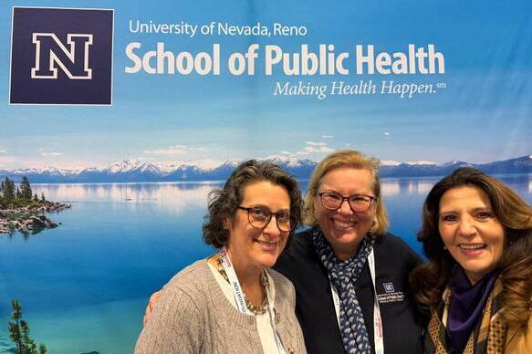 Three women pose for a photo in front of a banner of Lake Tahoe with "University of Nevada, Reno School of Public Health, Making Health Happen."