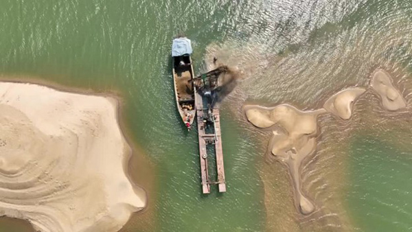An aerial view of a boat loaded with sand between two sandbars with a machine next to it.