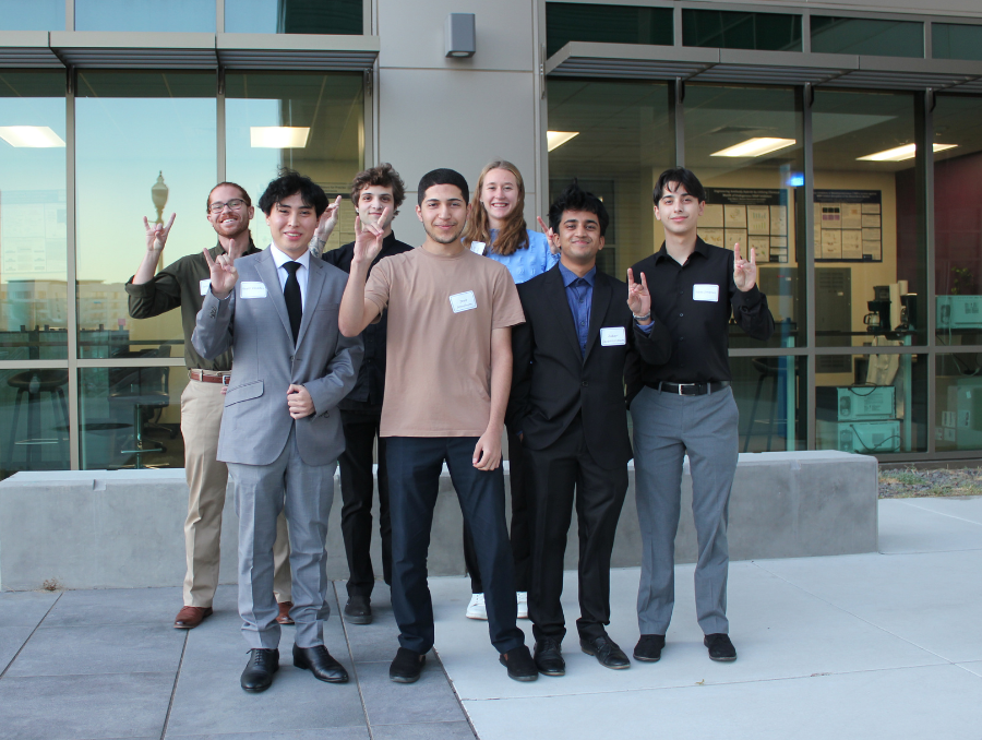 A group photo of engineering students pose together outside the university engineering building, holding up the Nevada Wolf Pack hand sign.