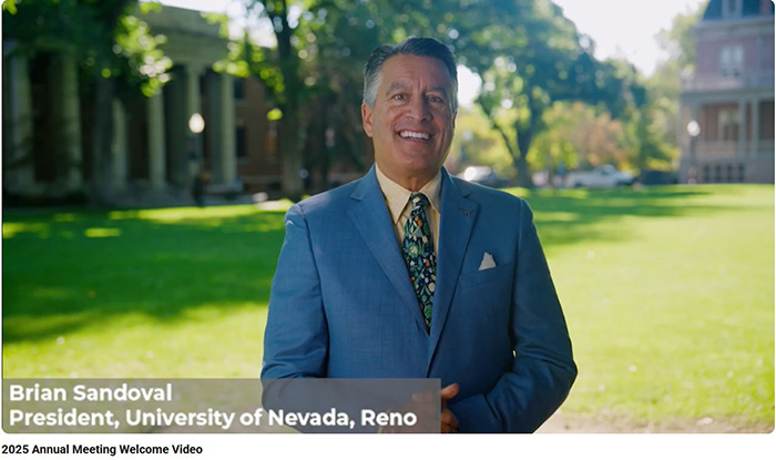 Brian Sandoval, President of the University of Nevada, Reno, smiling outdoors with campus buildings in the background.