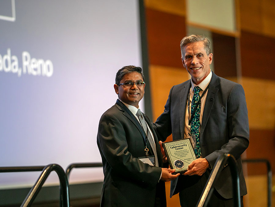 Two men in suits stand next to a podium holding a plaque.
