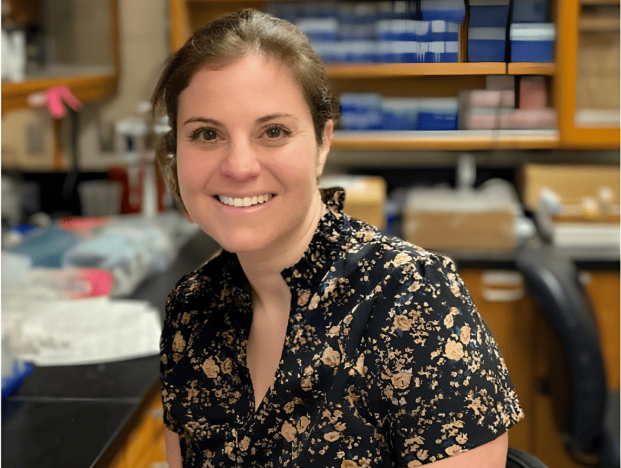 A smiling individual sitting in a laboratory setting.