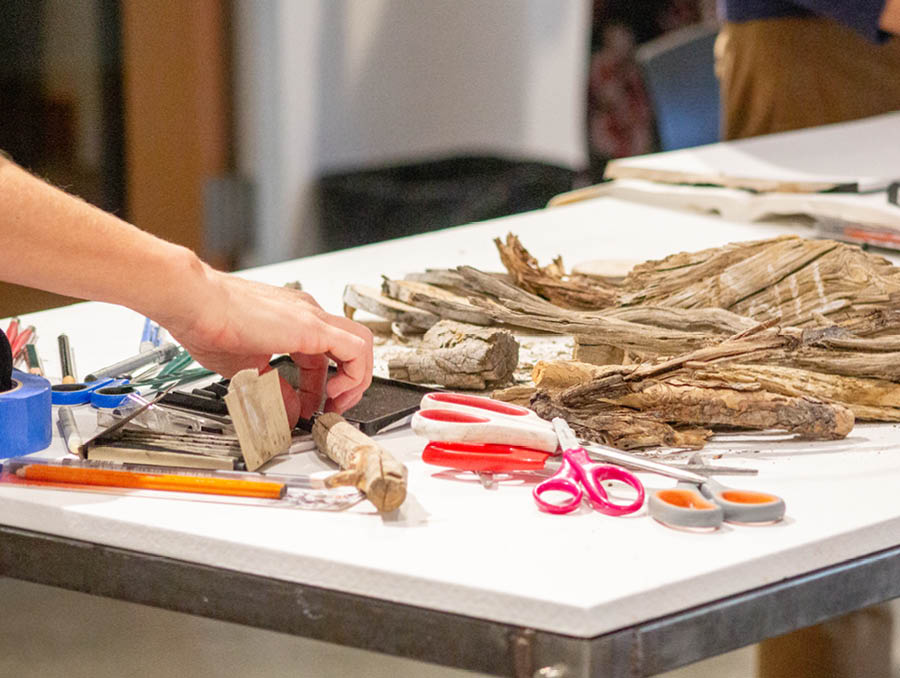 A hand grabbing art materials to draw the pieces of wood on the table.