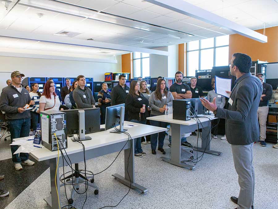Hanif Livani, standing in the foreground, speaks to a group of about 30 people gathered in a lab.