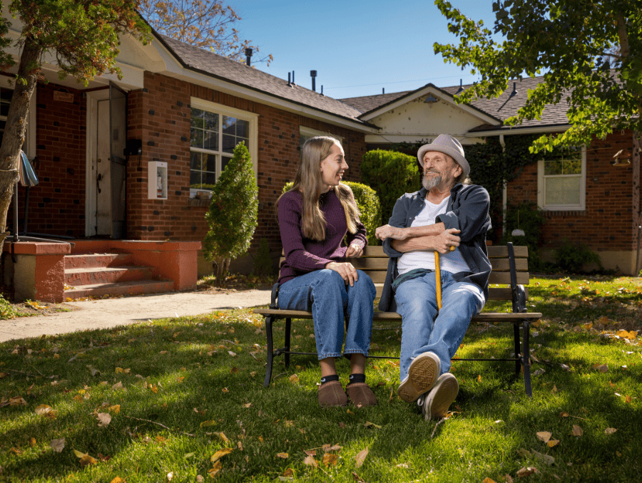 An older man sitting on a bench outside with a younger woman.