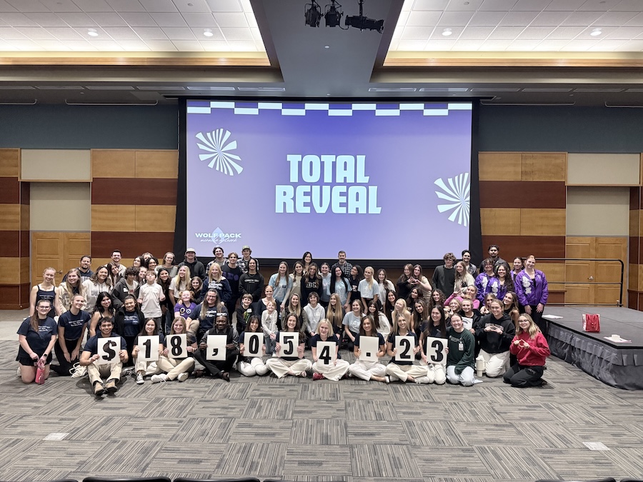 A large group of students, holding signs that read $18,054.23, sitting in front of a Presentation that reads "Total Reveal."