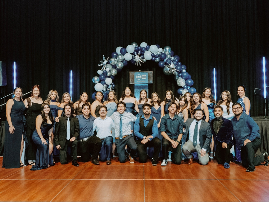 DFS faculty and mentors on stage in formal attire with a balloon arch behind them.