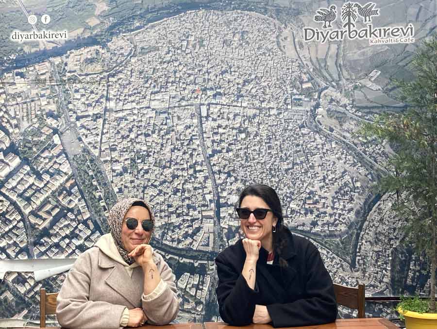 Two women sit at a table resting their chins on their hands in front of an aerial map.