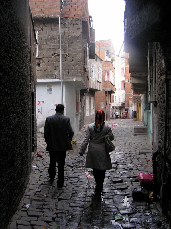 Two people walk in an alleyway over cobblestone streets.