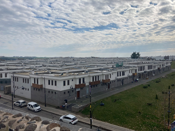 A photo taken above a housing development under a partly cloudy sky. The housing development is a repetitive series of two-story buildings.