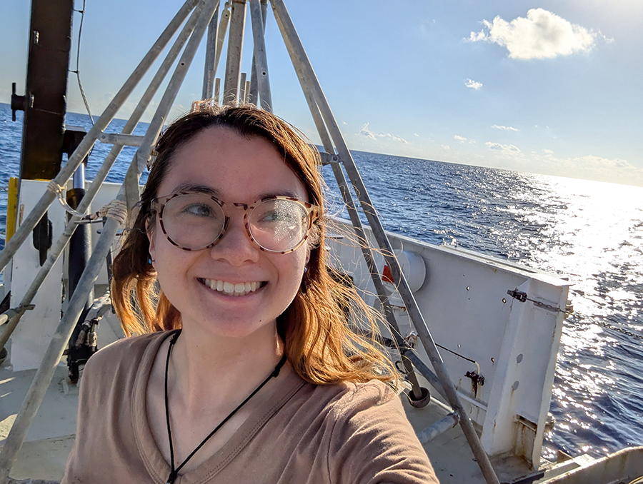 Hiroka Winter stands smiling on the deck of the research vessel with the ocean and sun behind her