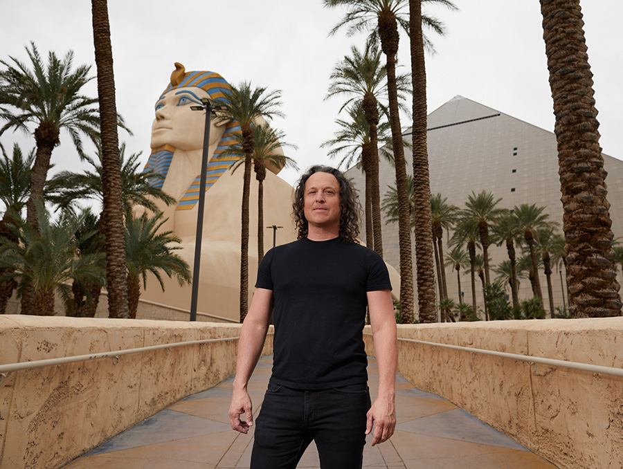 Jarret Keene stands in front of the Sphinx in Las Vegas. He is wearing a black short sleeve t-shirt and black pants.