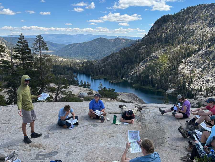 ODAL lecture on top of a boulder with a mountain view. Students are sprawled across rocks, listening.
