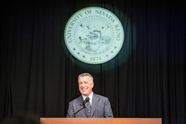 President Sandoval smiles at the crowd during the address with the State of Nevada Seal illuminated behind him.