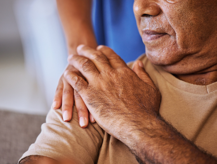 A person gently places their hand over another person’s hand resting on their shoulder.