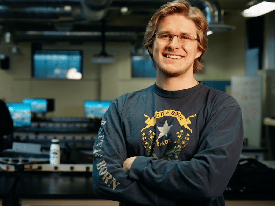 Carson Peterson in a computer lab, wearing a state of Nevada "battle born" shirt.