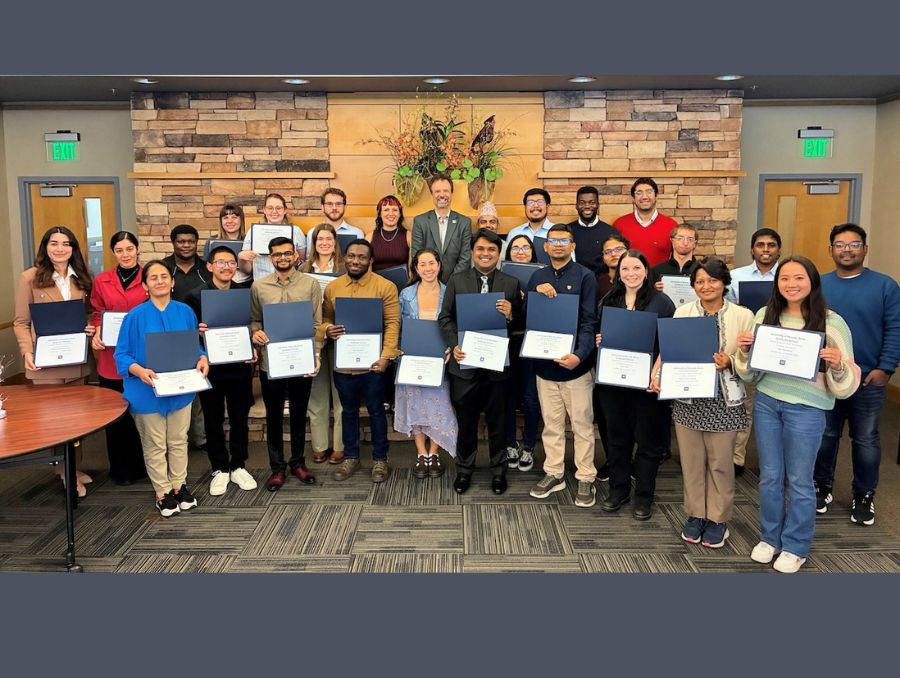 A large group of grad student recipients pose with Dean Kemmelmeier while holding their certificates.