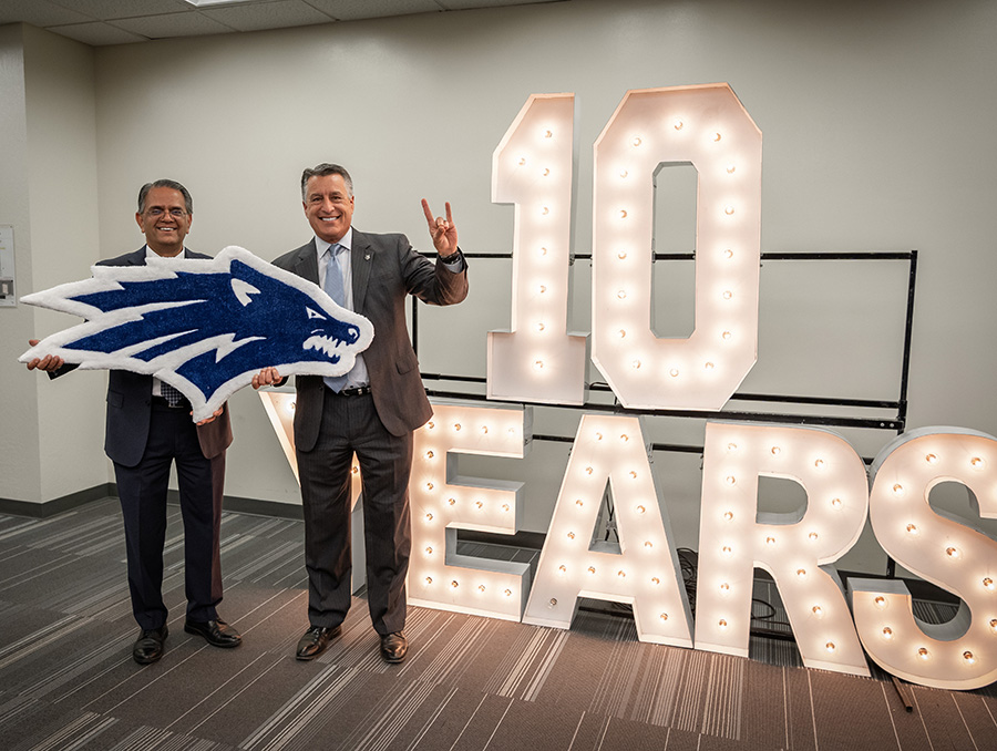 Mridul Gautam and Brian Sandoval hold a Wolf Pack rug and a in front of an illuminated "10 years" sign.