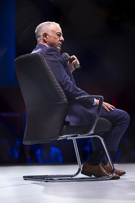 Nevada Governor Joe Lombardo sits on stage holding a microphone during a panel discussion.