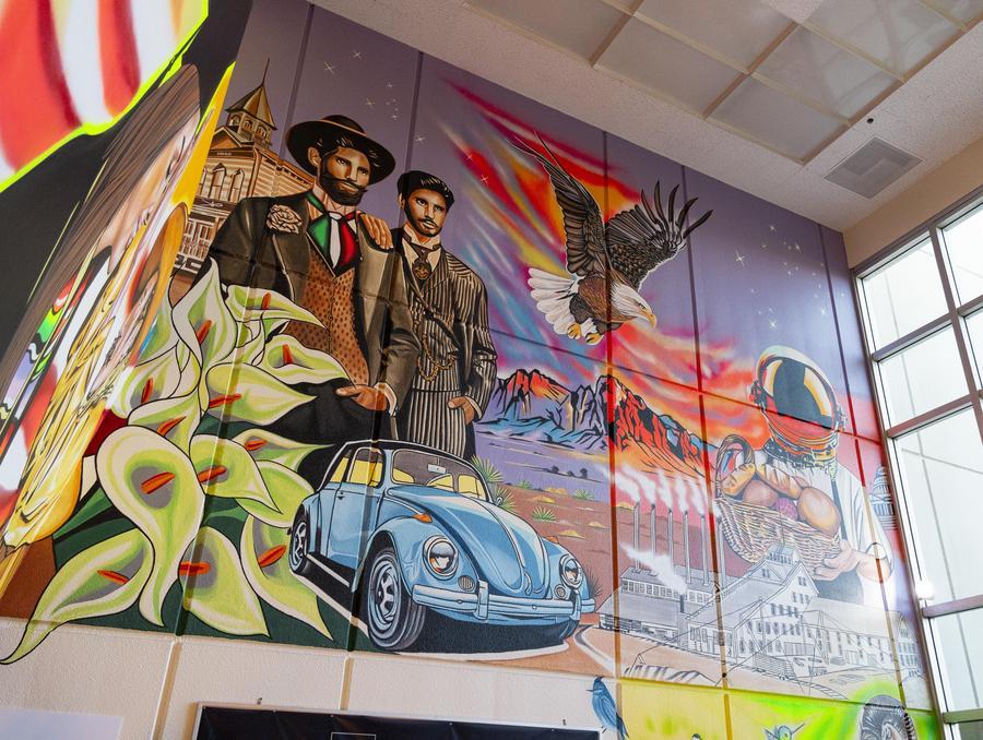 A panel of the mural depicting a blue slug bug Volkswagen car, two men looking into the distance, an eagle, mountains, a factory, and an astronaut carrying a bread basket.