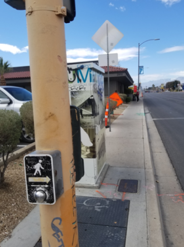 A sidewalk with a cross walk pole and close by a structure that looks like a booth.