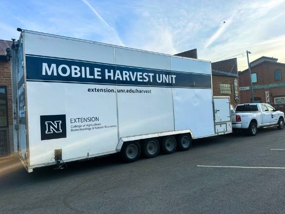 A trailer hooked to the back of a tow truck branded with Extension and with the words "Mobile Harvest Unit" on it.