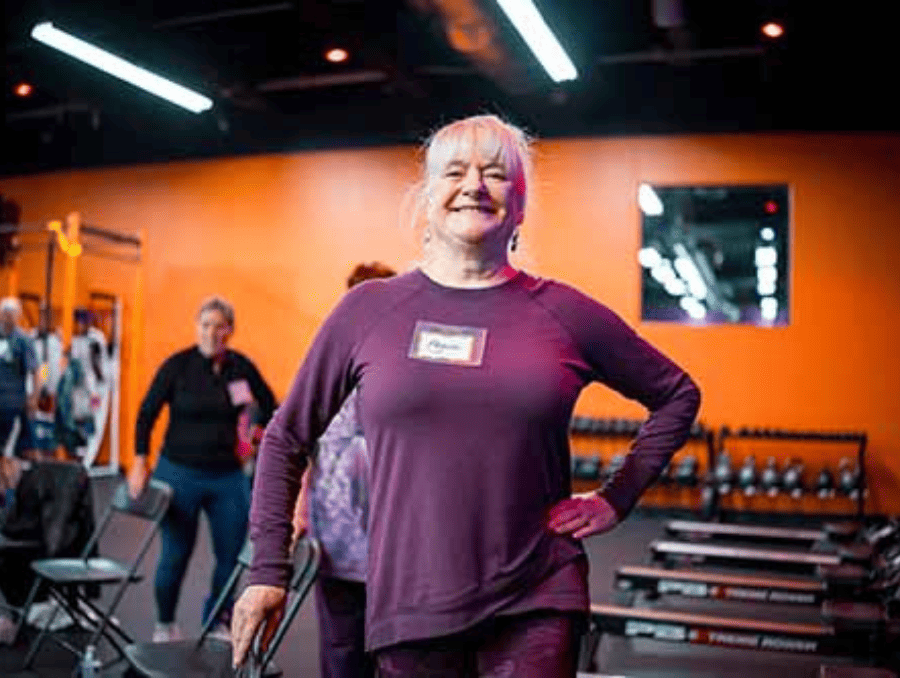 An older woman stretching in a gym with others.