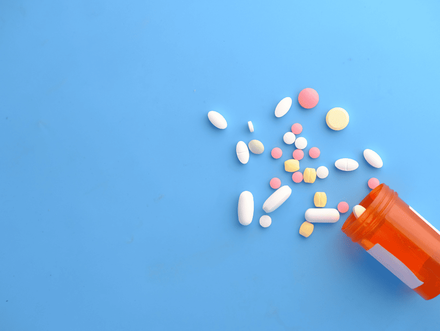 A pill bottle with medication falling out in a variety of colors and sizes. 