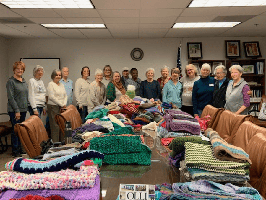 A group of older adults standing behind their hand-crafted crocheted and knitted creations.