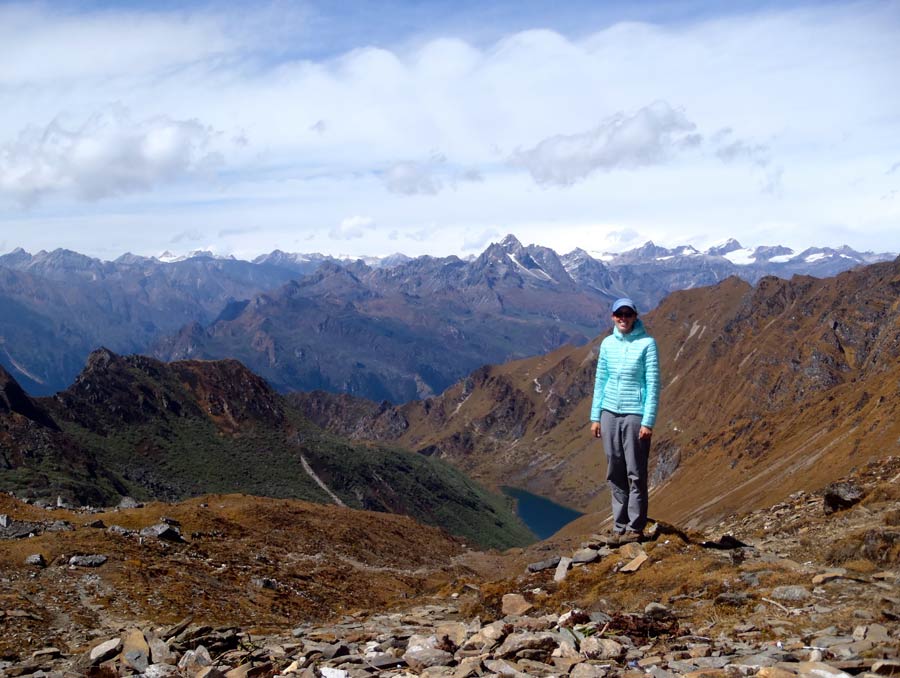 Stacia Gordon stands on a rocky outcropping overlooking a valley surrounded by stunning, snow-capped mountains.