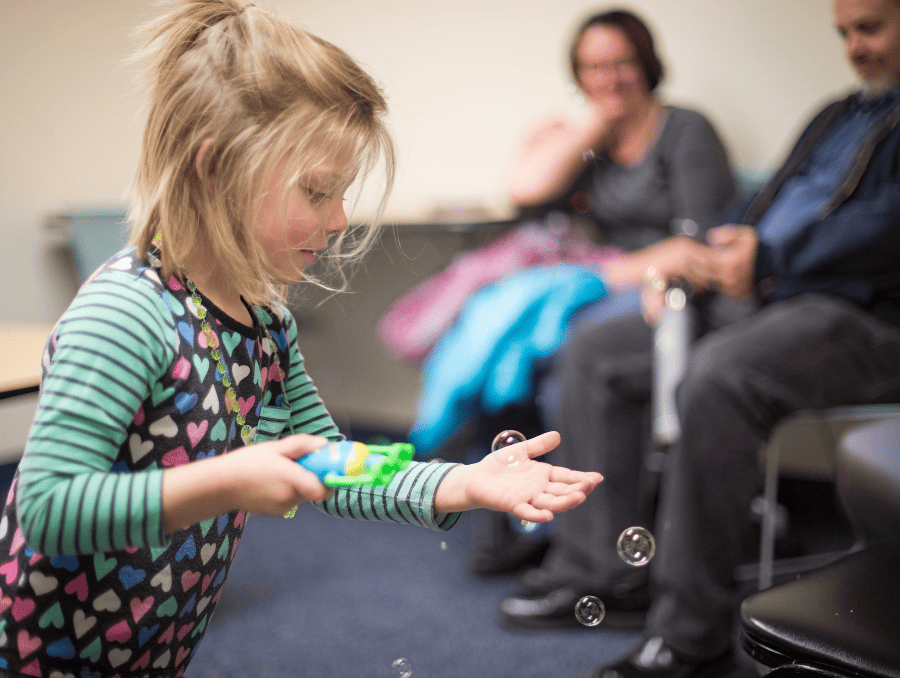 a child playing with bubbles with her parents behind her
