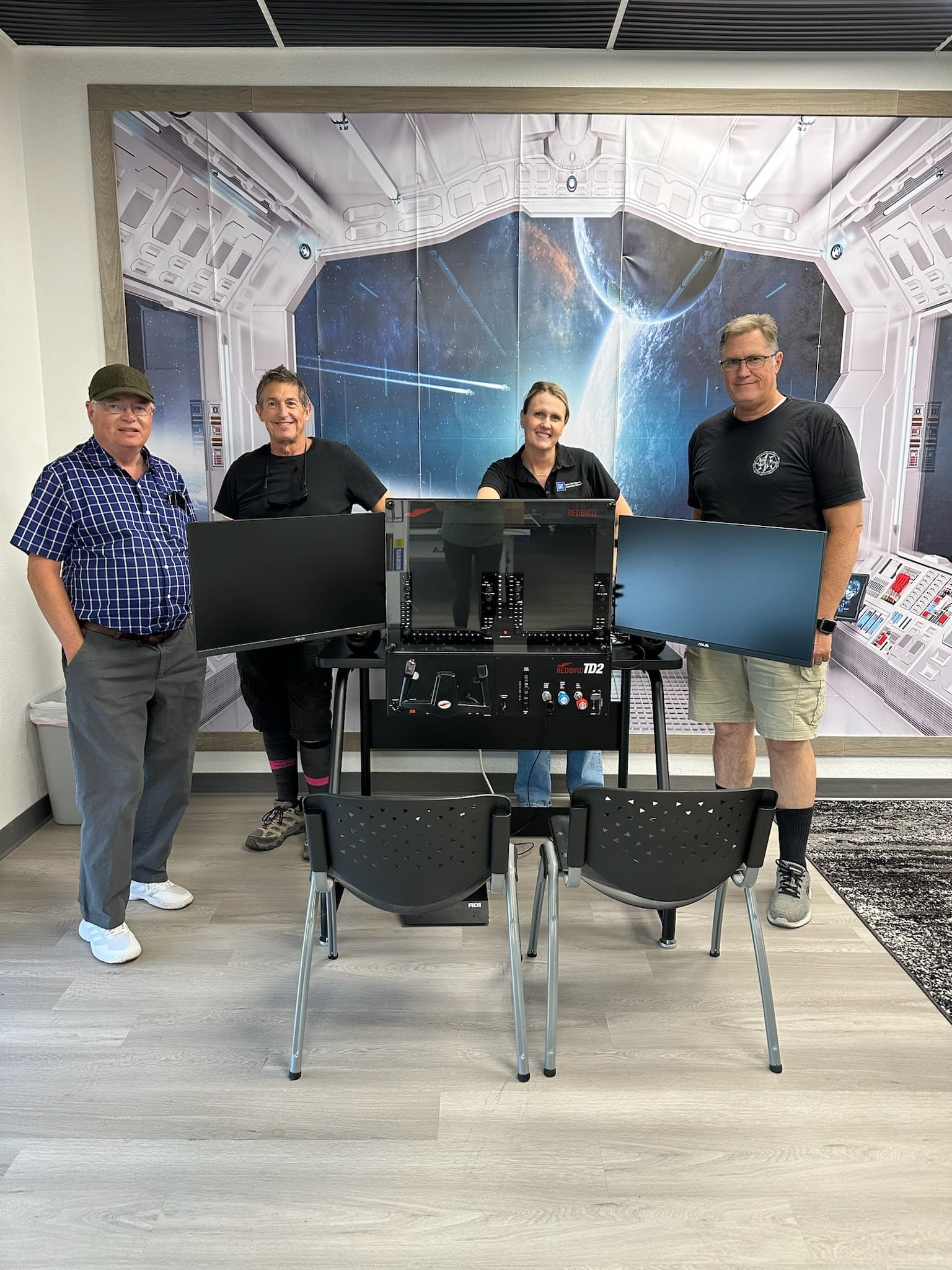 Three men and one woman standing behind three dashboard screens.