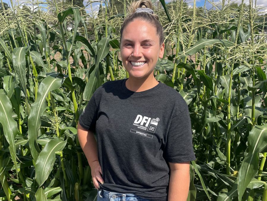 A smiling woman poses amid a backdrop of cornrows.