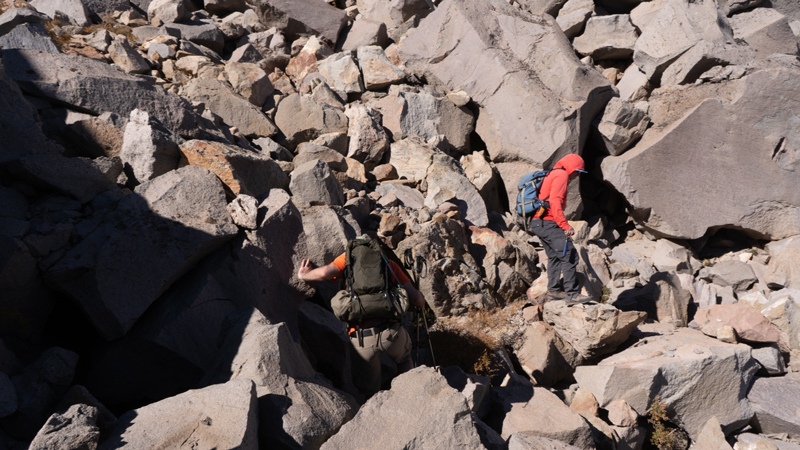 Two people scaling down rocky terrain among large boulders.