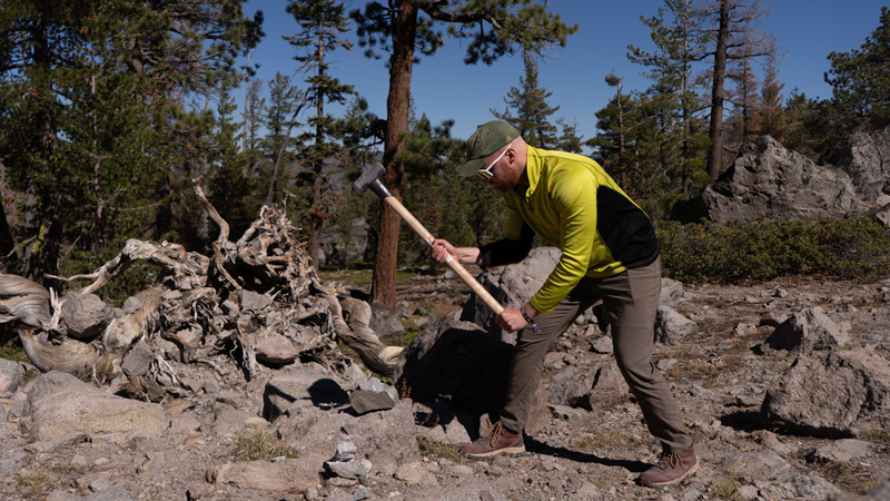 Jakob Scheel swings a large mallet, aiming for a rock.