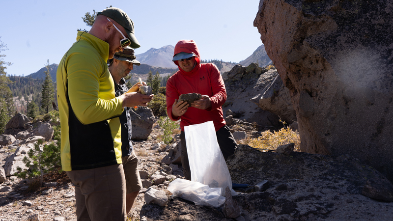 Researchers in the field holding rocks and discussing with one another.