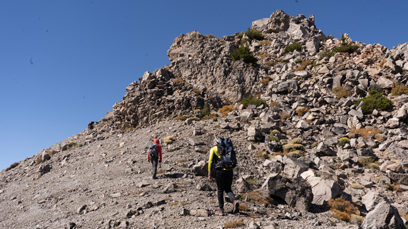 Two researchers climb a rocky mountain face.