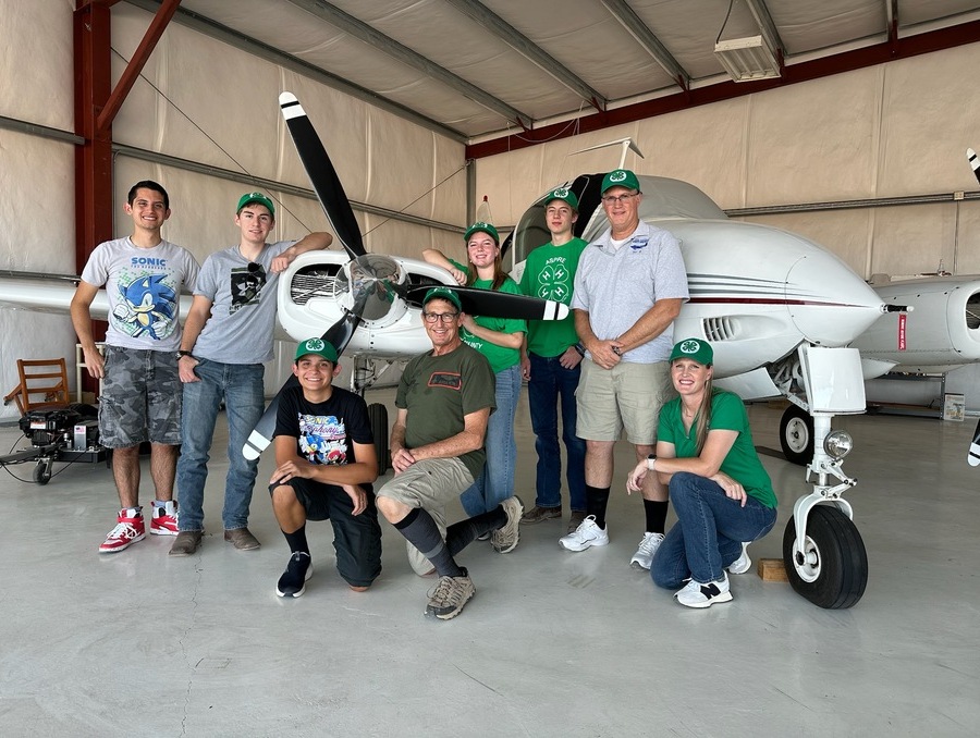 A group of men and women posing in front of a small plane. 