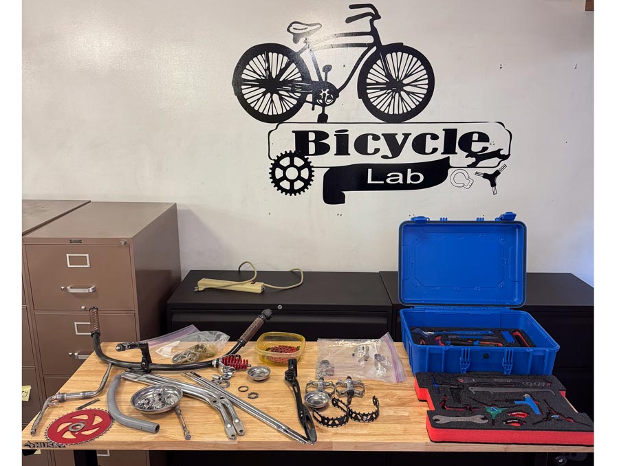 A table with a blue box and various tools in front of a whiteboard with a decal of a bike and text that reads, "Bicycle Lab".