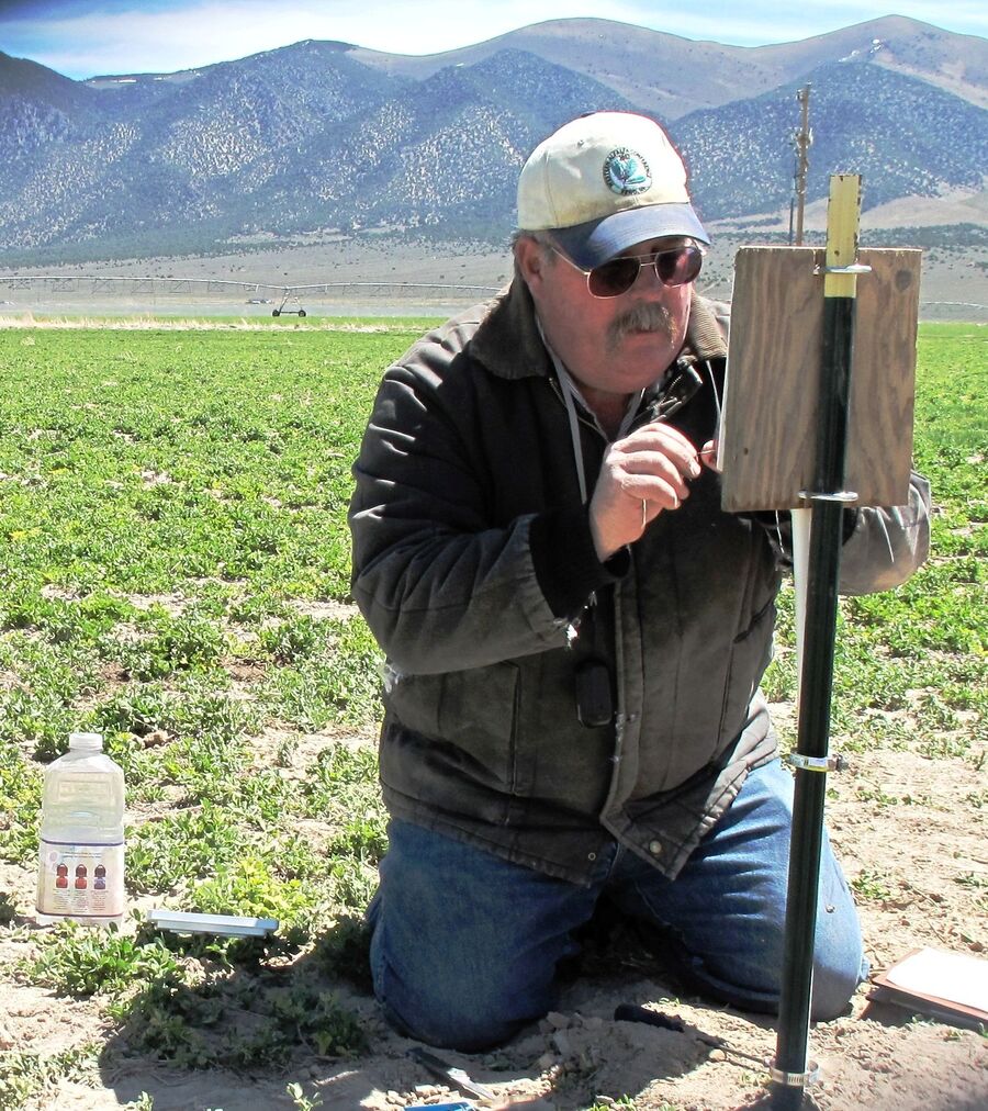 A man kneeling on the ground in a farm pushing an object onto a raised board.