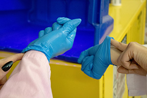 Two people’s hands in blue gloves, demonstrating the proper protocol for removing gloves. 