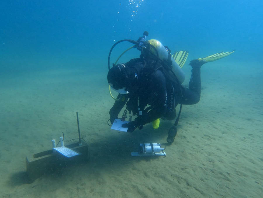 A person scuba diving collects samples from the sand at the bottom of Lake Tahoe.