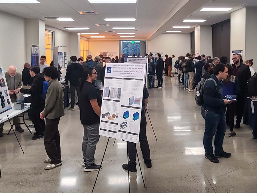 Students view booths in a hallway with a poster displaying a scientific project in the middle of the hall.