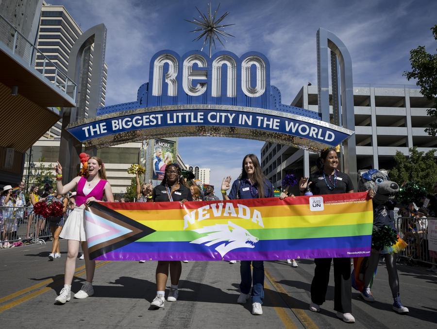 Students walking under the Reno arch, holding a Nevada logoed Pride Flag as they march.