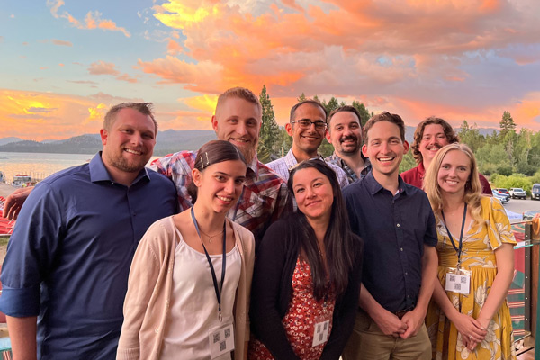 A group of people smile for a photo next to Lake Tahoe with a bright orange and yellow sunset behind them.