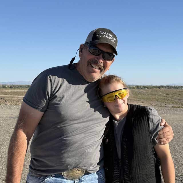 A smiling 4-H youth sporting protective eyewear and vest gives her 4-H leader a side hug.