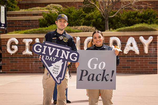 Two University Police officers stand smiling in front of balloons spelling out Giving Day, holding &ldquo;Giving Day&rdquo; and &ldquo;Go Pack!&rdquo; signs. 